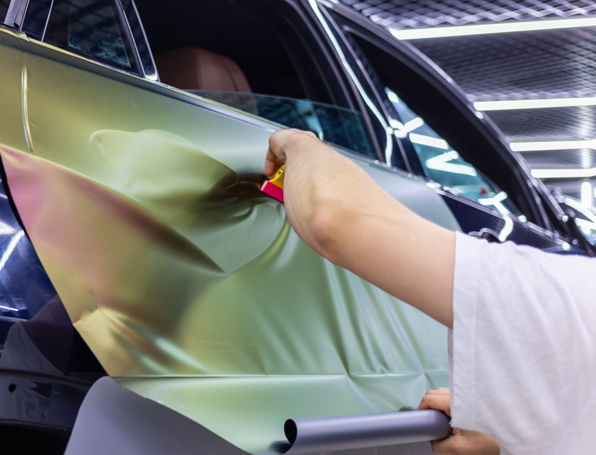 A specialist in wrapping a car with chameleon-colored vinyl film in the process of work. Car wrapping close-up.